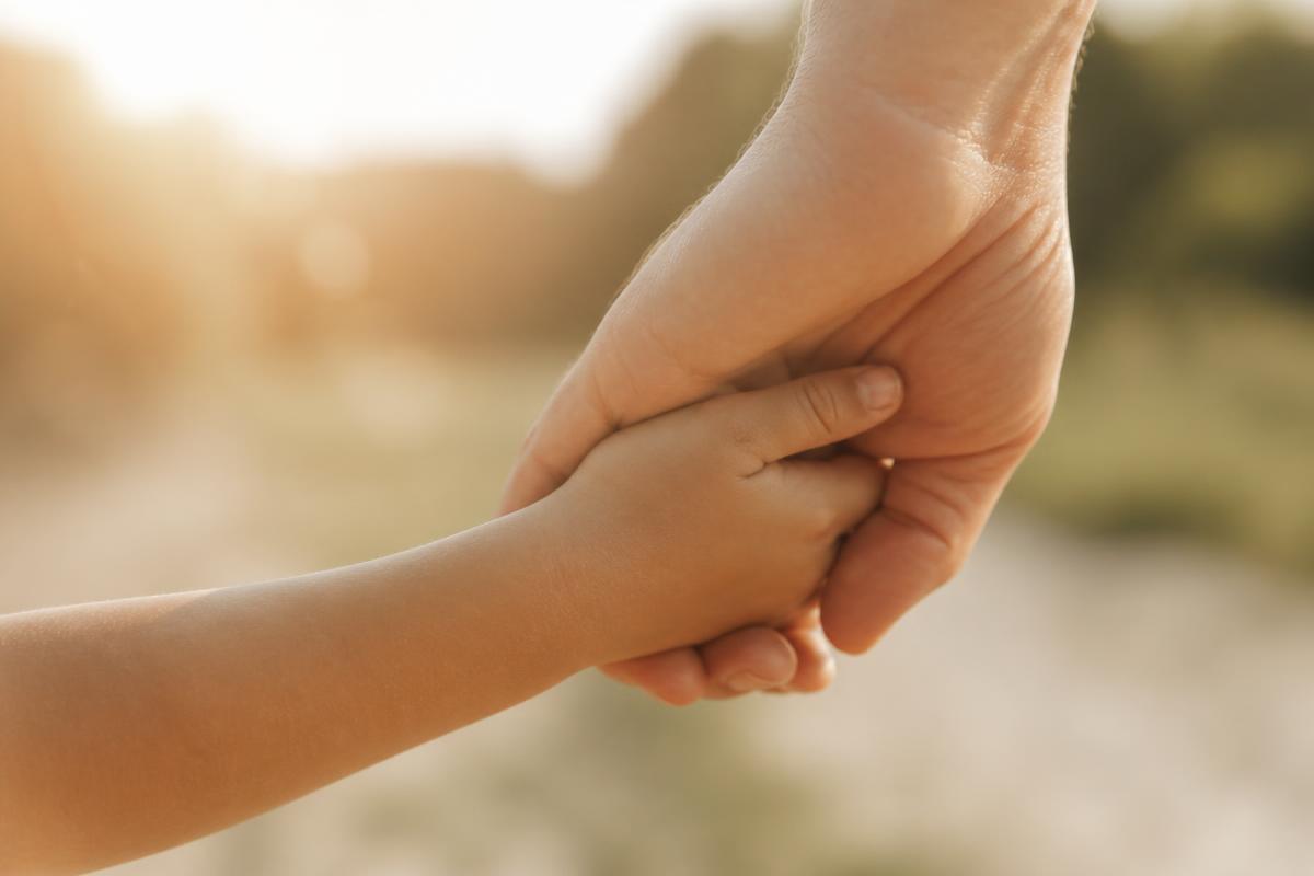 Een volwassen hand houdt de hand van een kind vast in warm licht